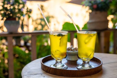 İki canlı sarı limonlu çay içeceği, ahşap bir tepside, nane yapraklarıyla süslenmiş ve pipetle servis edilen zarif bardaklarda oturur. Bu harika mekan DuJiangYan, Sichuan 'da büyüleyici bir kafede bulunuyor.