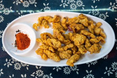 Beyaz bir tabakta bol miktarda kızarmış abur cubur sergilenir, altın kahverengi renk ve davetkar çıtır bir doku ile karakterize edilir. Ana yemeğin yanında, küçük bir kase canlı kırmızı tutar.