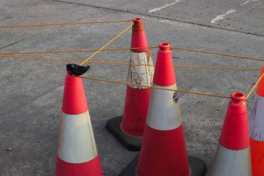 Alışveriş merkezinin otoparkında gri asfalt üzerinde beyaz ve turuncu çizgili bir grup trafik konisi.