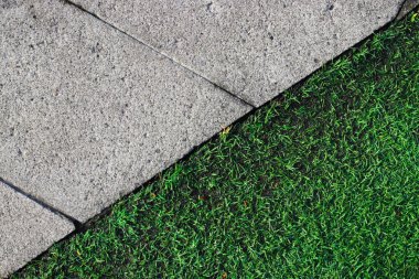 Yeşil çimenlikteki bir geçitte suni çim ve beton döşeme manzarası.