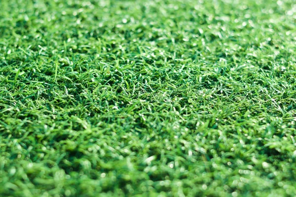 Green artificial turf close up with selective focus. Green artificial grass background with copy space.