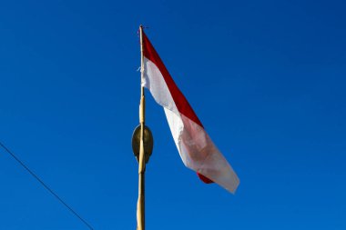 Sabahları açık mavi gökyüzüne karşı rüzgarda dalgalanan bambu direğindeki Endonezya bayrağı.