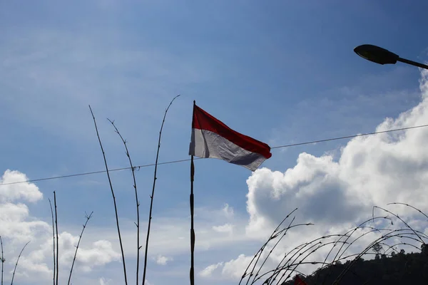 Indonesia flag on a bamboo pole waving in the wind against clear blue sky in the morning.