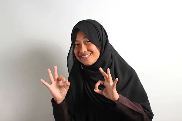 身穿黑色头巾或头巾的漂亮年轻亚洲女孩在看着白色背景的相机时 用手语做出了不错的手势 — 图库照片