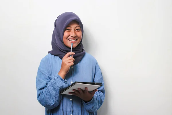 Uśmiechnięta Młoda Azjatka Uczennica Hidżabie Zainteresowana Myśleniem Trzymając Książkę Długopis — Zdjęcie stockowe