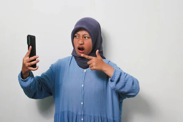 Zdezorientowana Młoda Azjatka Hidżabie Ubrana Luźną Koszulę Trzymająca Telefon Białym — Zdjęcie stockowe