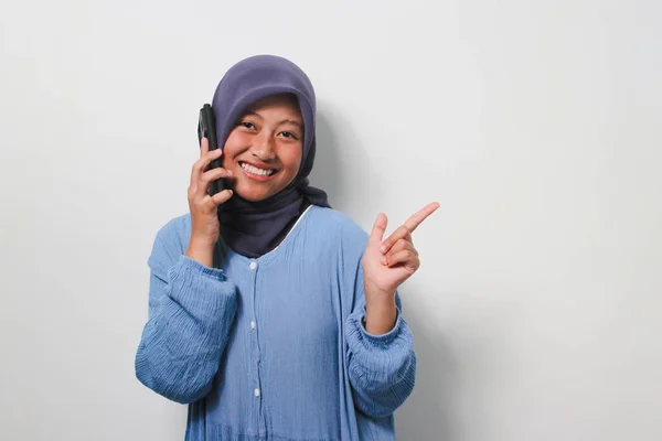 평상복 차림으로 히잡을 아시아 소녀는 배경에 떨어져 공간을 가리키면서 전화를 — 스톡 사진