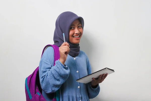 聪明的亚洲女学生 头戴头巾 手持笔和书本 凝视着被白色背景隔离的相机 — 图库照片