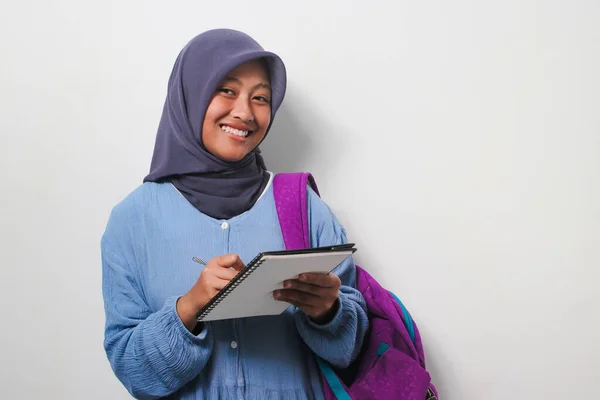 Stock image Clever young Asian girl student in hijab holding a pen and book smiling and looking at camera isolated on white background.