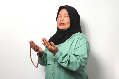 Orta yaşlı Asyalı kadınlar siyah başörtüsü takıyor ve günlük gömlekler giyip Tanrı 'ya dua ediyor, el kaldırıyor ve beyaz arka planda izole edilmiş tespih tutuyor..