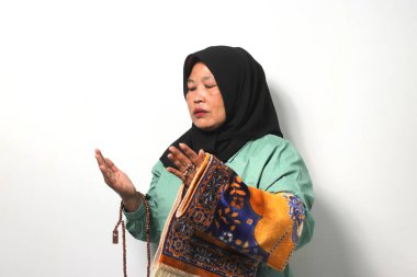 Orta yaşlı Asyalı kadınlar siyah başörtüsü takıyor ve günlük gömlekler giyip Tanrı 'ya dua ediyor, dua eden el kaldırıyor ve beyaz arka planda izole edilmiş tespih ve oyuncu paspası tutuyor..