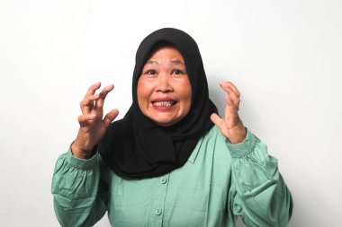 Kızgın Orta yaşlı, siyah tesettürlü ve günlük gömlekli Asyalı kadınlar beyaz arka planda izole edilmiş kameraya bakarken ellerini kaldırdılar..