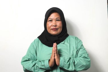 Gülümseyen Orta yaşlı Asyalı kadınlar siyah başörtüsü takıyor ve bayram hediyesi olarak el kol hareketi yapıyor beyaz arka planda izole edilmiş kameraya bakarken..