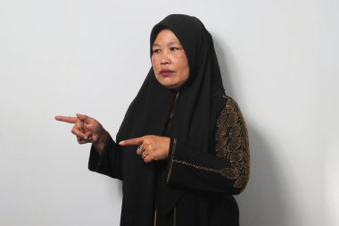 Mutsuz orta yaşlı siyah tesettürlü Asyalı kadınlar ve abaya, beyaz arka planda izole edilmiş fotokopi alanının solunu işaret ediyorlar..