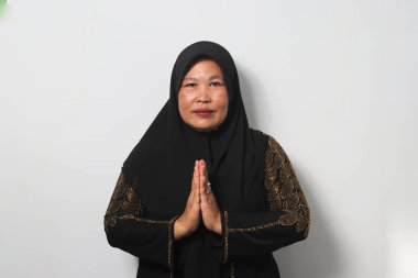 Gülümseyen Orta yaşlı Asyalı kadınlar siyah tesettür ve abaya giyerek, bayram kutlamaları yaparken beyaz arka planda izole edilmiş kameraya bakıyorlar..
