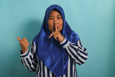 Orta yaşlı, mavi tesettürlü bir Asyalı kadın boş fotokopi alanını parmağıyla işaret ediyor. Sessiz olur ya da sessiz bir jest yapar. Mavi arka planda izole edilmiş gizli bir satış teklifini anlatır.