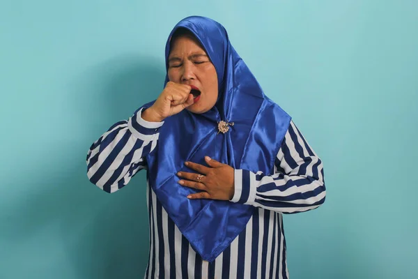 一名身穿蓝色头巾和条纹衬衫的体弱多病的亚洲中年妇女站在蓝色的背景下 满嘴咳嗽着 — 图库照片