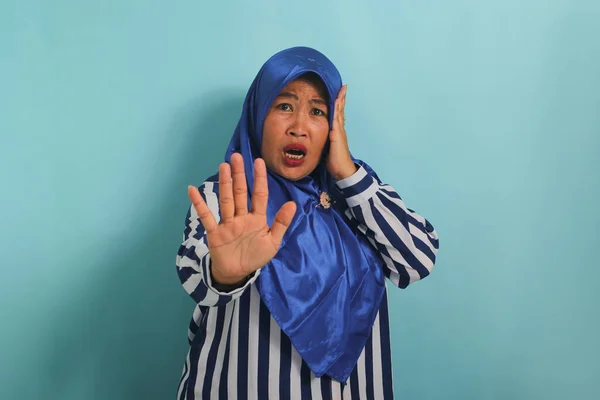 一名身穿蓝色头巾和条纹衬衫的吓坏了的亚洲中年妇女站在蓝色背景下 吓得直喘气 — 图库照片