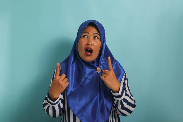 Zaskoczona Azjatka Średnim Wieku Niebieskim Hidżabie Koszuli Paski Wskazuje Palcami — Zdjęcie stockowe