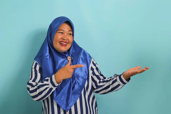 Azjatka Średnim Wieku Niebieskim Hidżabie Pasiastej Koszuli Wskazującej Otwartą Dłoń — Zdjęcie stockowe
