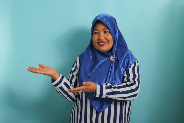 Azjatka Średnim Wieku Niebieskim Hidżabie Pasiastej Koszuli Wskazującej Otwartą Dłoń — Zdjęcie stockowe