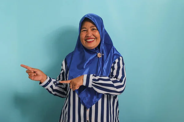 Entuzjastyczna Azjatka Średnim Wieku Niebieskim Hidżabie Pasiastej Koszuli Wskazuje Lewo — Zdjęcie stockowe