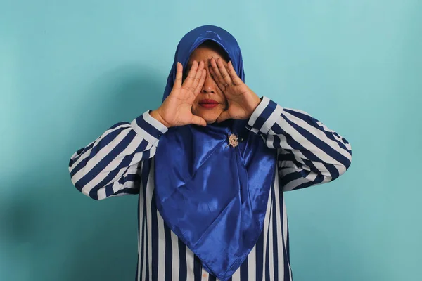 青いヒジャーブとストライプのシャツを着たアジア系の中年女性は 青い背景を背景に立ちながら指で三角形を形成します — ストック写真