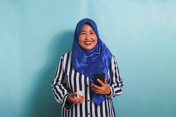 Uśmiechnięta Azjatka Średnim Wieku Niebieskim Hidżabie Koszuli Paski Telefonem Komórkowym — Zdjęcie stockowe