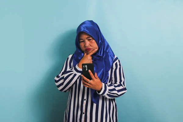 Azjatka Średnim Wieku Niebieskim Hidżabie Koszuli Paski Poważnie Myśli Trzymając — Zdjęcie stockowe