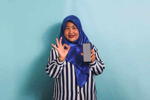 Возбужденная Азиатка Средних Лет Синем Хиджабе Полосатой Рубашке Держит Телефон — стоковое фото