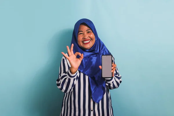 Возбужденная Азиатка Средних Лет Синем Хиджабе Полосатой Рубашке Держит Телефон — стоковое фото