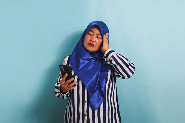 Znudzona Azjatka Średnim Wieku Niebieskim Hidżabie Koszuli Paski Trzyma Telefon — Zdjęcie stockowe
