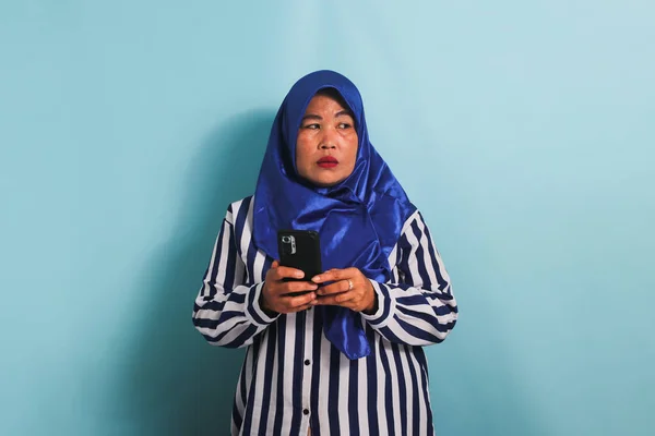Znudzona Azjatka Średnim Wieku Niebieskim Hidżabie Koszuli Paski Trzyma Telefon — Zdjęcie stockowe