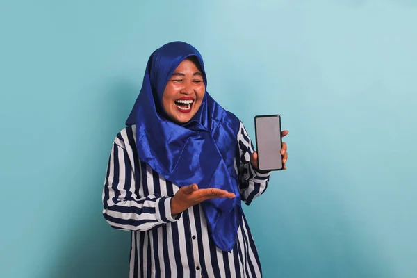 Возбужденная Азиатка Средних Лет Синем Хиджабе Полосатой Рубашке Показывает Телефон — стоковое фото