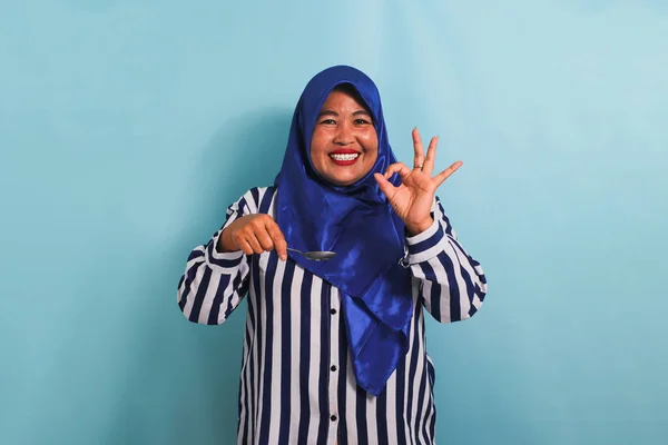 Podekscytowana Azjatka Średnim Wieku Niebieskim Hidżabie Pasiastej Koszuli Degustuje Jedzenie — Zdjęcie stockowe