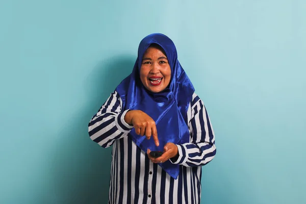 Azjatka Średnim Wieku Niebieskim Hidżabie Koszuli Paski Podkręca Głośność Telewizora — Zdjęcie stockowe