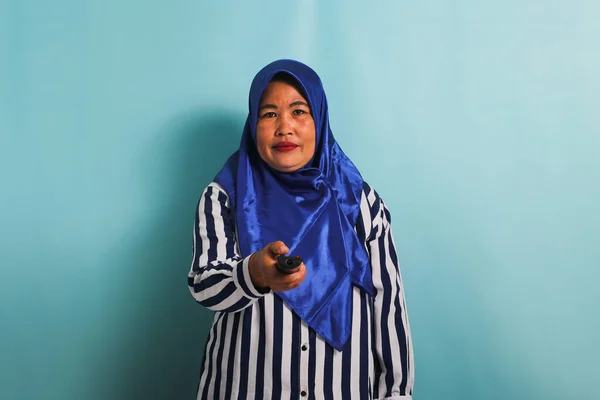 Azjatka Średnim Wieku Niebieskim Hidżabie Pasiastej Koszuli Trzyma Pilota Wskazuje — Zdjęcie stockowe