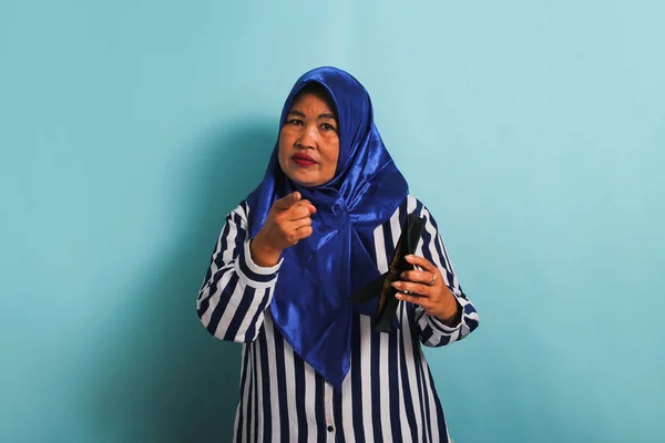 一名身穿蓝色头巾和条纹衬衫的亚洲中年妇女拿着一只空皮夹指着相机 看上去很沮丧 她被蓝色背景隔离了 — 图库照片