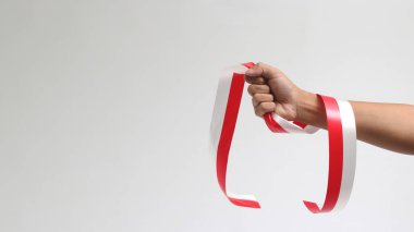 Elinde kırmızı ve beyaz bir kurdele tutan bir adam. Beyaz bir arkaplanda izole edilmiş, Endonezya Bağımsızlık Günü konseptini temsil ediyor.