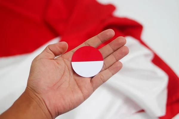 Hand holding Indonesia flag against blurred red and white flag background isolated on a white background