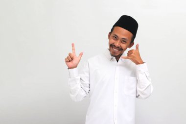 Songkok, peci ya da kopiah giyen heyecanlı Endonezyalı genç adam beyaz bir arka planda izole edilmiş boş fotokopi alanını işaret ederken beni arayıp jest yapıyor.