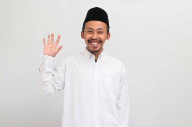 Endonezyalı genç adam, bir Songkok, peci, veya kopiah giyiyor, jest yapıyor Merhaba, Greeting One, beyaz arka planda soyutlanmış