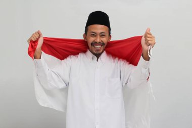 Endonezya 'nın heyecanlı genç bir adamı Endonezya Bağımsızlık Günü' nü kutlamak için 17 Ağustos 'ta beyaz arka planda izole edilmiş bir Endonezya bayrağı tutuyor.