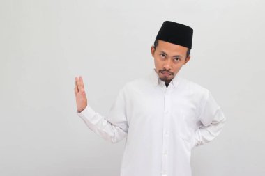 Songkok, peci ya da kopiah giyen, ciddi bir Endonezyalı genç adam, beyaz arka planda durması, reddetmesi ya da yasaklaması için bir uyarı işareti gösteriyor.