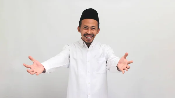 stock image Smiling young Indonesian man wearing a songkok or peci or kopiah, is beckoning with both hands, offering a hug with a come here gesture, inviting, welcoming, isolated on a white background