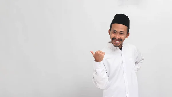 年轻的印尼男人 穿着歌舞剧 山核桃或Kopiah 把大拇指指向空旷的复制空间 被白色的背景隔开 — 图库照片