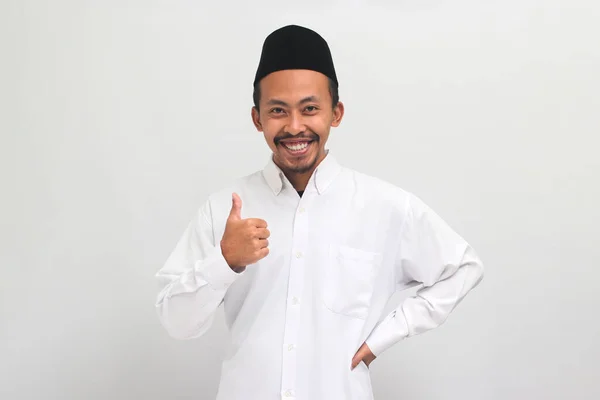 有自信的印度尼西亚年轻人身穿红衫 山核桃或Kopiah 竖起大拇指 表达了积极的评价和良好的反馈 与白人背景隔离 — 图库照片