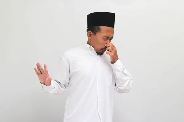 無視されたインドネシア人男性は 曲を着て ピシア またはピシアを着て 彼の鼻に指で息を止め 彼は何か臭い 嫌悪感 耐え難い匂いを白い背景に孤立させます — ストック写真