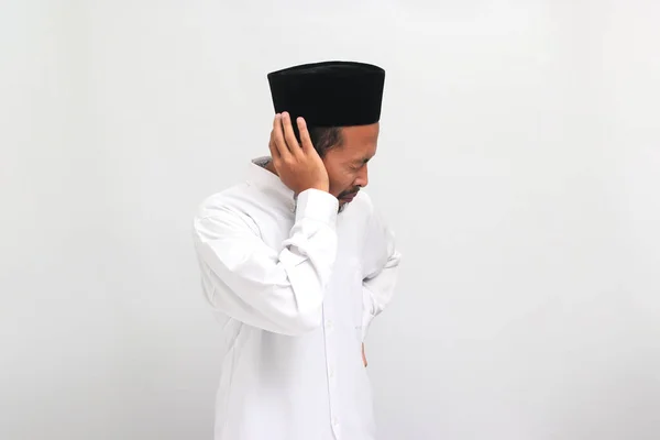 若いインドネシア人男性は ソングコック ピッチ またはコピアを着用して 耳の近くに手を保持し 耳鳴り 吐き気 騒音による疲労 白い背景に隔離されています — ストック写真