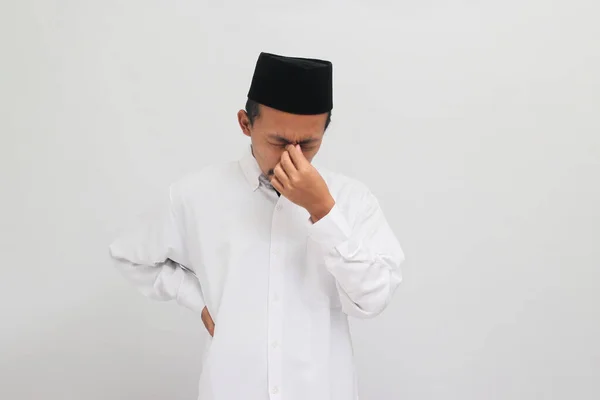 若いインドネシア人男性 ソングコックを着て Peci またはコピア 彼の鼻をピンチ 頭痛に苦しんで 過労と片頭痛のためにストレスを感じます 白い背景に孤立しました — ストック写真